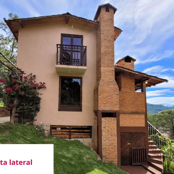 Vista lateral de la cabaña, con la chimenea de ladrillo y el balcón