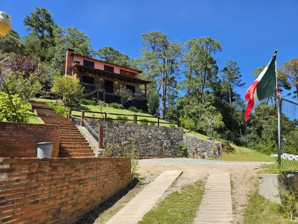 La cabaña entre los pinos, con la bandera de México en el jardín